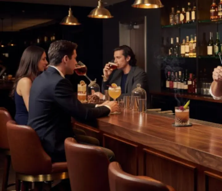 Handcrafted cocktail on a smoked glass table in a warm, amber-lit lounge.